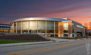 Modern, curved glass building with a gray facade at sunset.