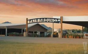 Fair Grounds archway over a road with buildings and parked trucks under a colorful sunset sky.