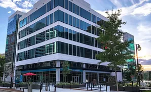 Modern glass office building with a tree in front, reflecting the sky.