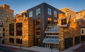 Modern building with stone and dark tile facades, large windows, and a glass entrance, illuminated by golden sunset light.