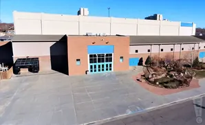 Large tan building with a brick entrance featuring blue doors and windows.