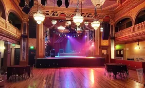 An empty concert hall with a stage, tables, and ornate decor.