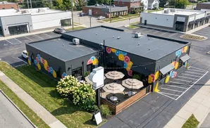 Aerial view of a dark gray building with a colorful donut mural and an outdoor patio with umbrellas.