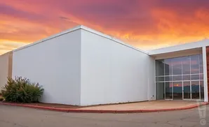 A modern building with large windows stands against a vibrant sunset sky.