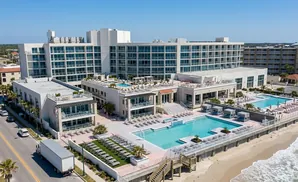 Aerial view of a modern beachfront hotel with multiple pools, lounge chairs, and ocean views.