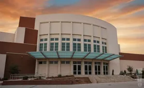 Modern building with curved facade and large windows under a dramatic sunset sky.