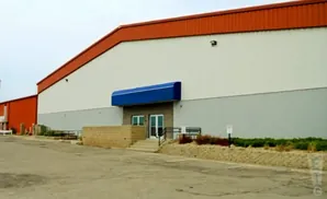 A large industrial building with an orange roof, white upper walls, and gray lower walls.