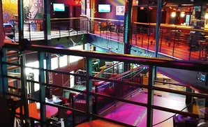 Interior view of a multi-level bar/club with railings, stairs, and neon lighting.