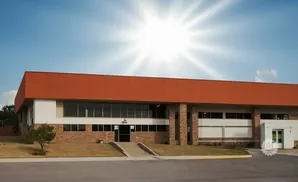 Modern building with orange and white facade, large windows, and stone accents under a bright sun.