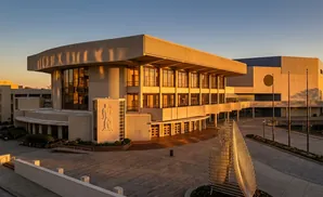 Modern building complex with large windows and geometric facade elements, bathed in golden hour light.
