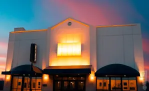 Exterior of a modern building with a marquee and illuminated windows at sunset.