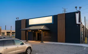 A modern building with a large illuminated sign, dark brick walls, and a covered entrance.