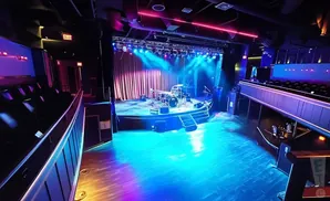 An empty concert hall stage set with drums and colorful stage lights.