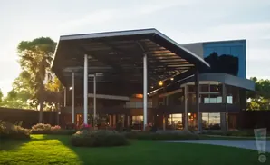 Modern building with large overhang and glass windows, surrounded by lush green lawn and flowering bushes.