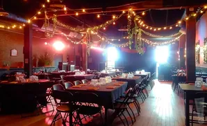 A dimly lit event space with tables set for dining, adorned with fairy lights and hanging plants.