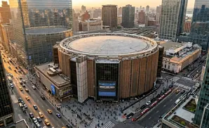 Aerial view of Madison Square Garden in New York City at sunset, with surrounding skyscrapers and street traffic.