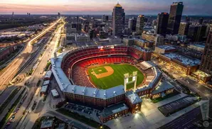 Aerial view of a baseball stadium at dusk, with city skyline and illuminated highways.