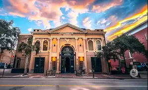 A tan building with arched windows and doors, under a colorful sunset sky.