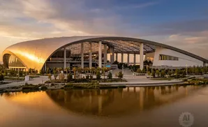 SoFi Stadium at sunset, with a reflective lake in the foreground and golden light illuminating the stadium's roof.