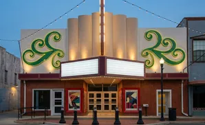 A vintage movie theater with neon green scrolls and marquee signs at dusk.