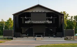 Outdoor concert stage with large screens, speakers, and lighting rig.