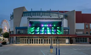 An outdoor stage with colorful lights in front of an entertainment venue, with a Ferris wheel in the background.