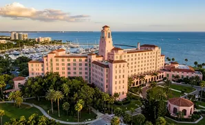 An aerial view of a pink hotel with a tower, overlooking a marina and the ocean.
