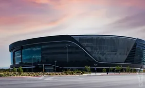 Allegiant Stadium, home of the Las Vegas Raiders, with a modern black exterior under a pink sky.