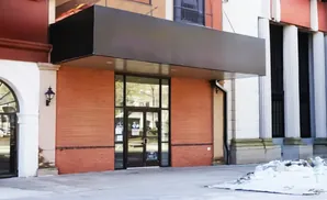 A modern storefront with a large black awning over brick walls and glass doors, framed by white columns and an arched entrance.