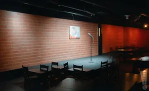 Comedy club stage with brick wall, microphone, and tables.