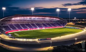 Nighttime view of a brightly lit soccer stadium with purple seating and a green field.