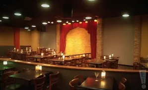 An empty comedy club with tables and chairs, featuring a brick stage with red curtains.