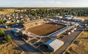 Aerial view of a rodeo arena with grandstands, surrounded by houses and trees.
