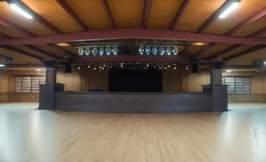 An empty ballroom with a stage, wooden floor, and ceiling lights.