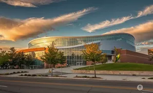 Modern curved building with glass facade, trees, and a dramatic sunset sky.