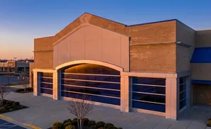 Modern building with large arched windows at sunset, reflecting the sky and parking lot.