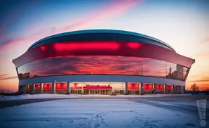 Modern stadium at sunset with red lighting and reflections in the glass exterior, surrounded by snow.