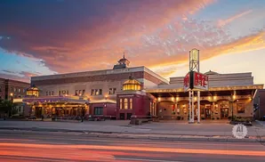 Evening view of a grand theater with illuminated marquees and a colorful sunset sky.