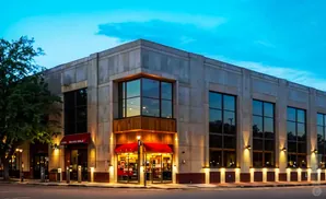 A modern stone building with large windows and red awnings at dusk.
