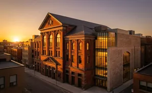 Sunset illuminates a brick building with classical and modern additions in an urban setting.