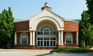 A modern brick building with a large arched entrance and windows, flanked by green trees.