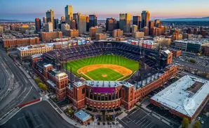 Aerial view of a baseball stadium with a city skyline and mountains in the background.