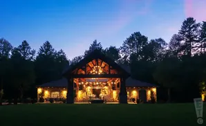 Rustic lodge with warm lights at dusk, surrounded by trees and a manicured lawn.