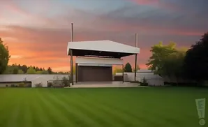 An outdoor stage with a white roof stands on a manicured lawn under a colorful sunset sky.