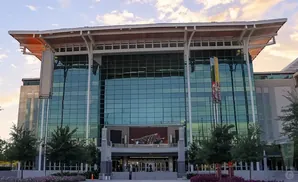Modern building with a glass facade and a large roof overhang, with trees and flowers in the foreground.
