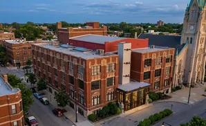 Aerial view of a brick building next to a church with a clock tower.
