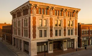 An ornate brick and stone building with ornate details stands on a street corner at sunset.