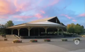 An outdoor pavilion with a white roof and open sides, set against a sky with pink and blue clouds at dusk.