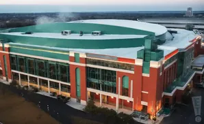 Aerial view of a large, modern stadium with a green roof and red brick exterior.