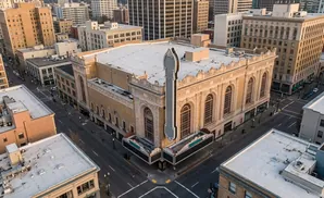 Aerial view of a grand, ornate theater with a large marquee, surrounded by city buildings.